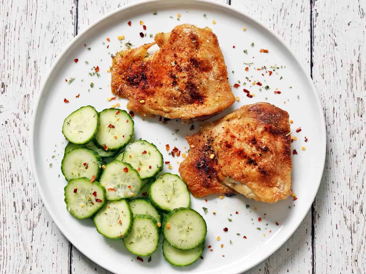 Cucumber vinegar salad is served as a side dish to crispy chicken thighs.