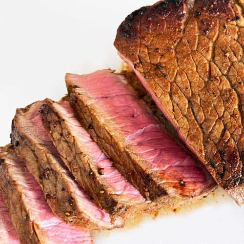 London broil steak, sliced, on a white cutting board.