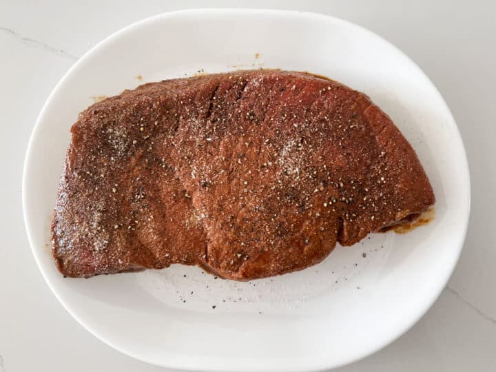 A London broil steak is seasoned with salt and pepper.