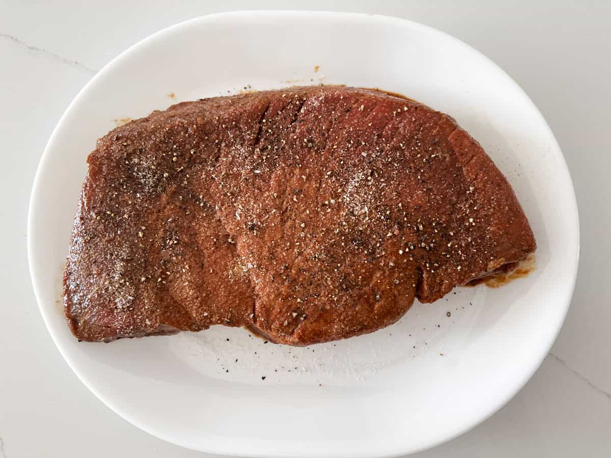 A London broil steak is seasoned with salt and pepper.