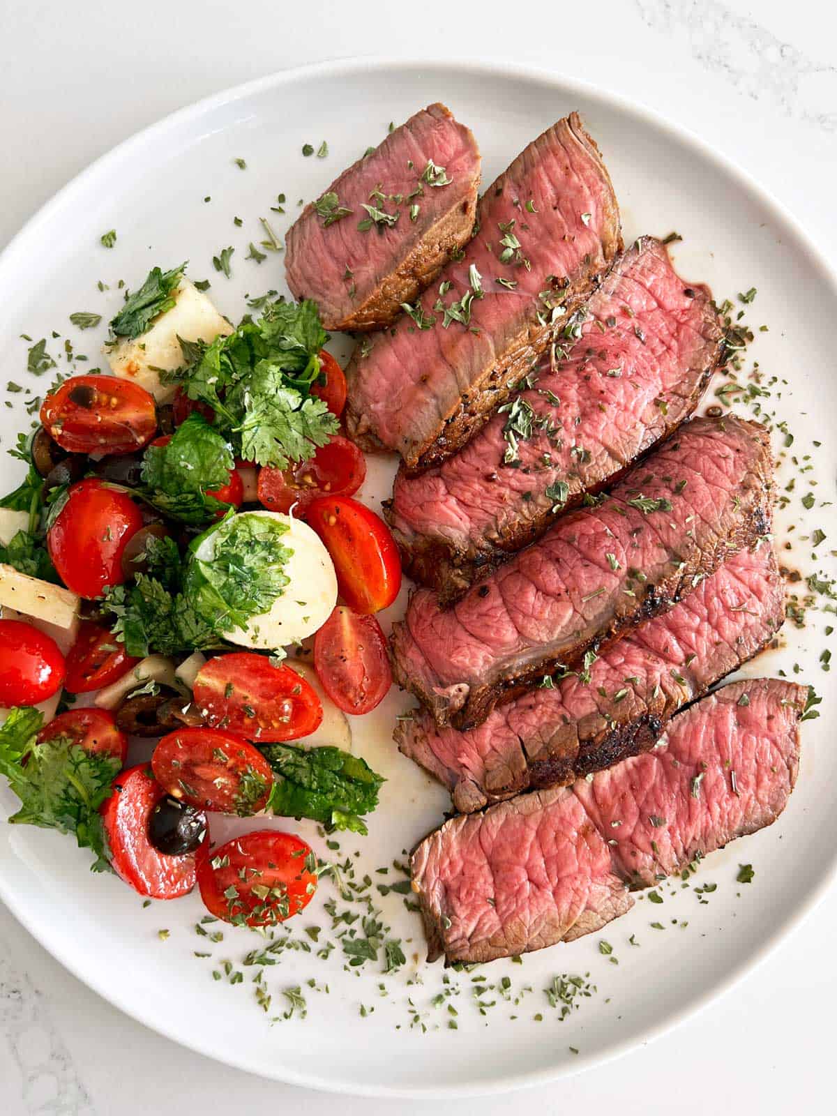 Slices of London Broil are served on a white plate with a side salad.