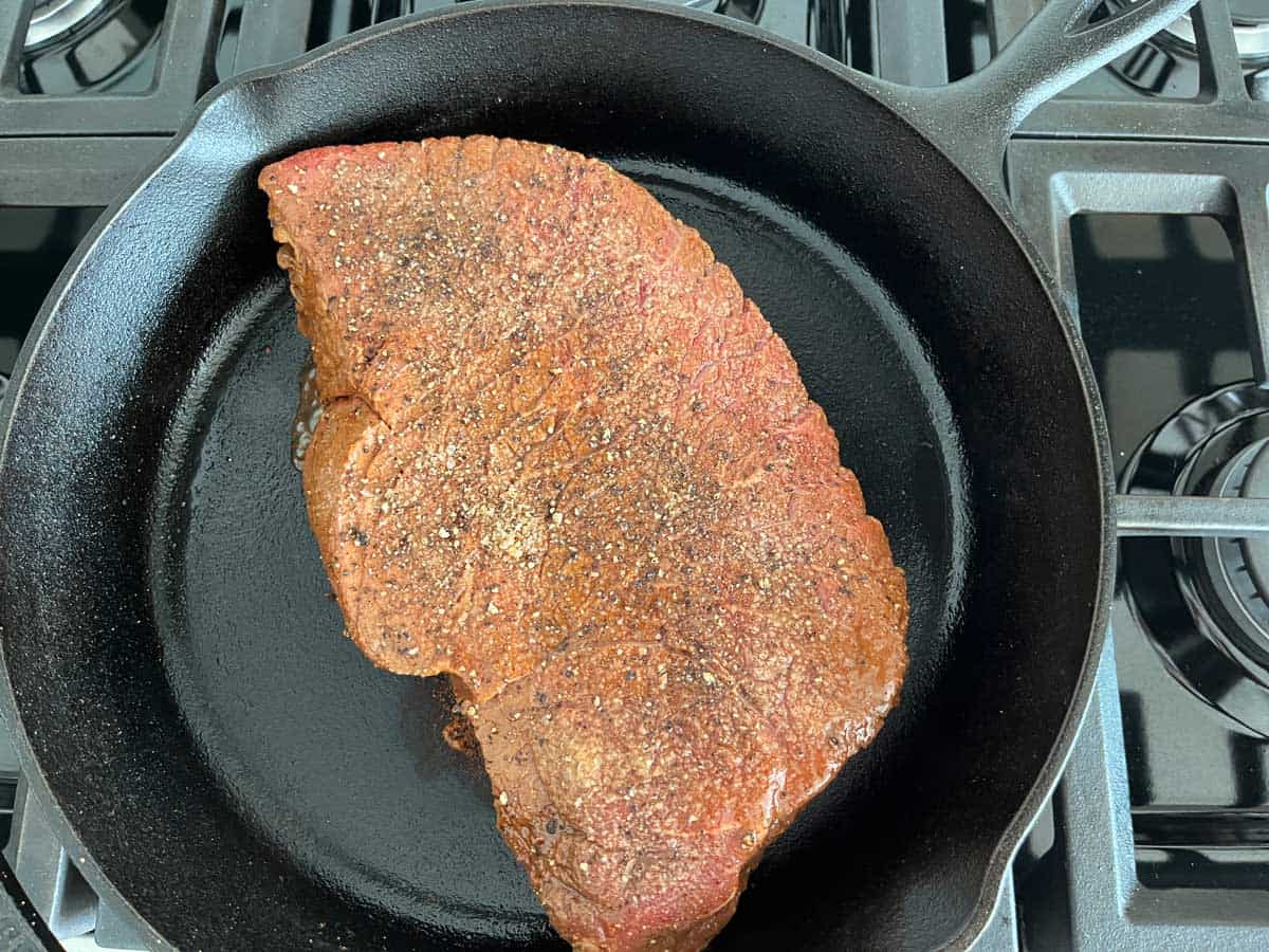 Cooking the London broil on the first side on a cast-iron skillet.