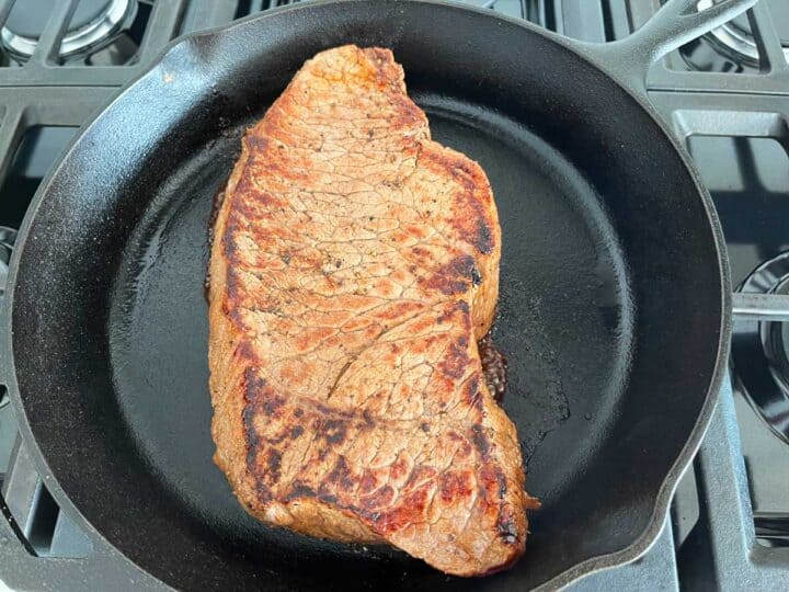 Cooking the London broil on the second side in a cast-iron skillet.