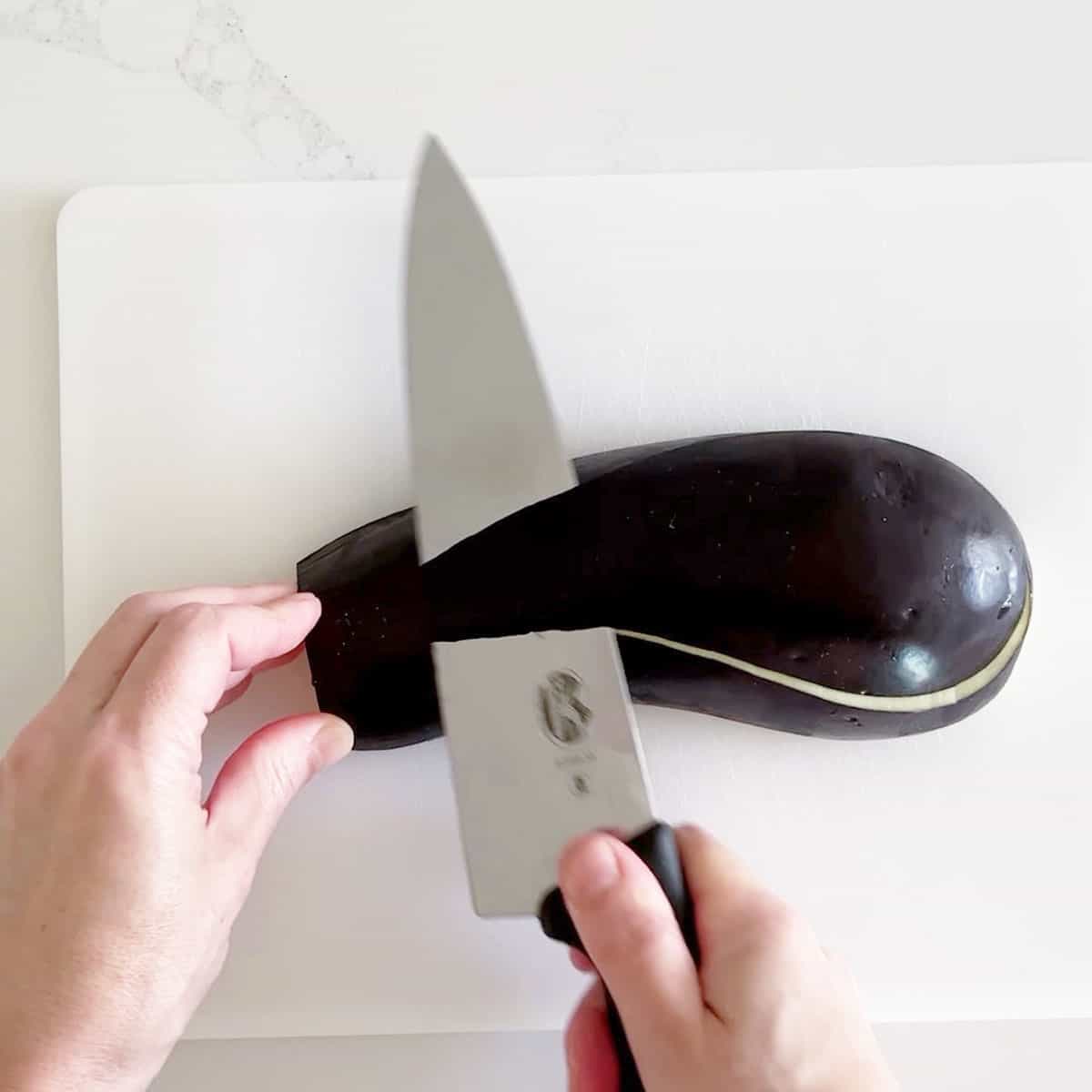 Slicing a thin strip off the rounded edges of the eggplant.