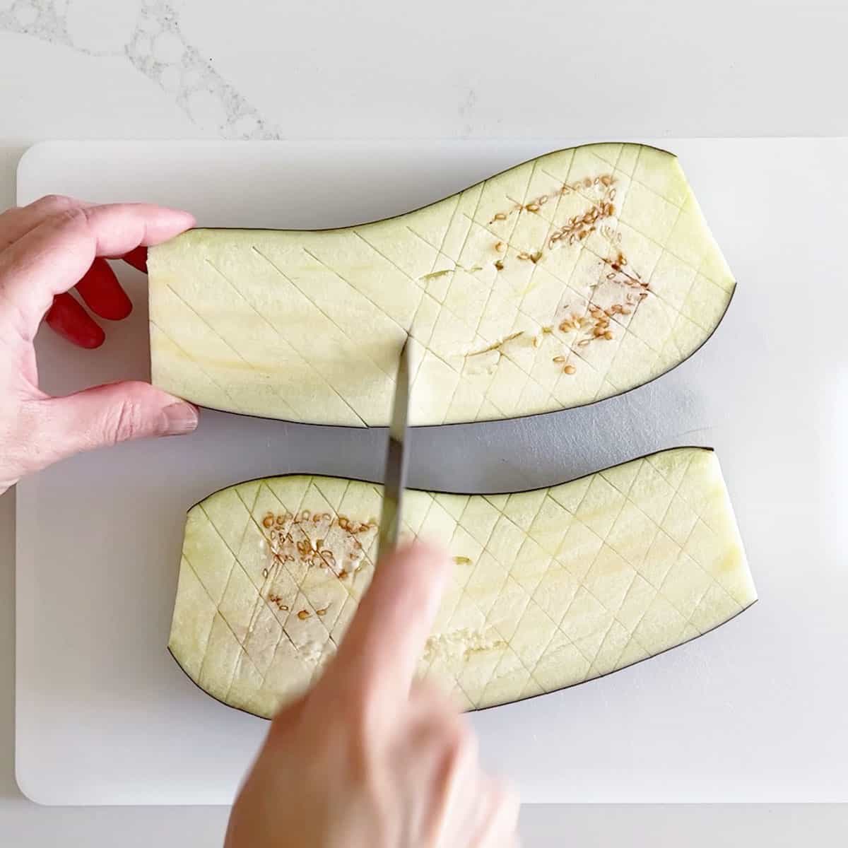 Making shallow cuts in a crosshatch pattern on the flesh side of the eggplant.