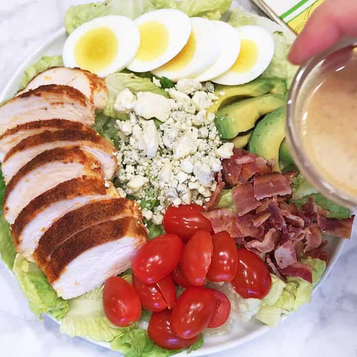 Drizzling the Cobb salad with the dressing.