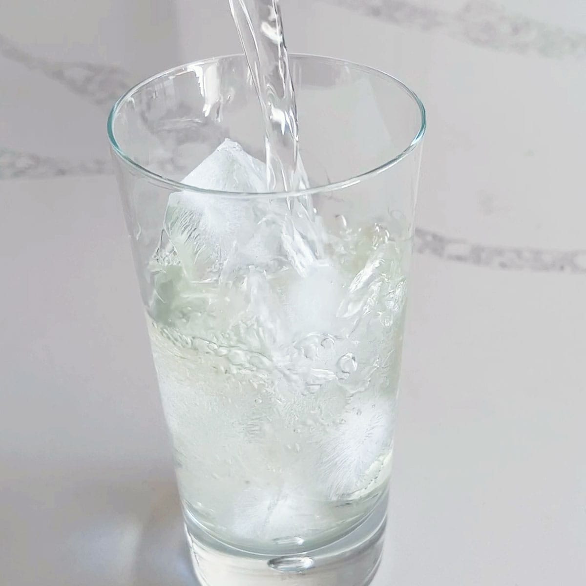 Pouring mint tea on ice cubes in a tall glass.