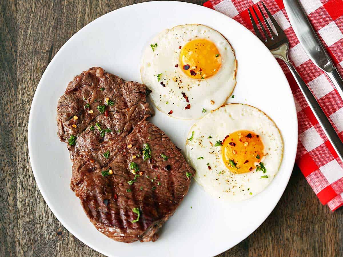 Steak and eggs are served on a white plate.