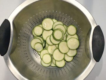 Salting the zucchini slices. Water drops are visible on the zucchini surface.