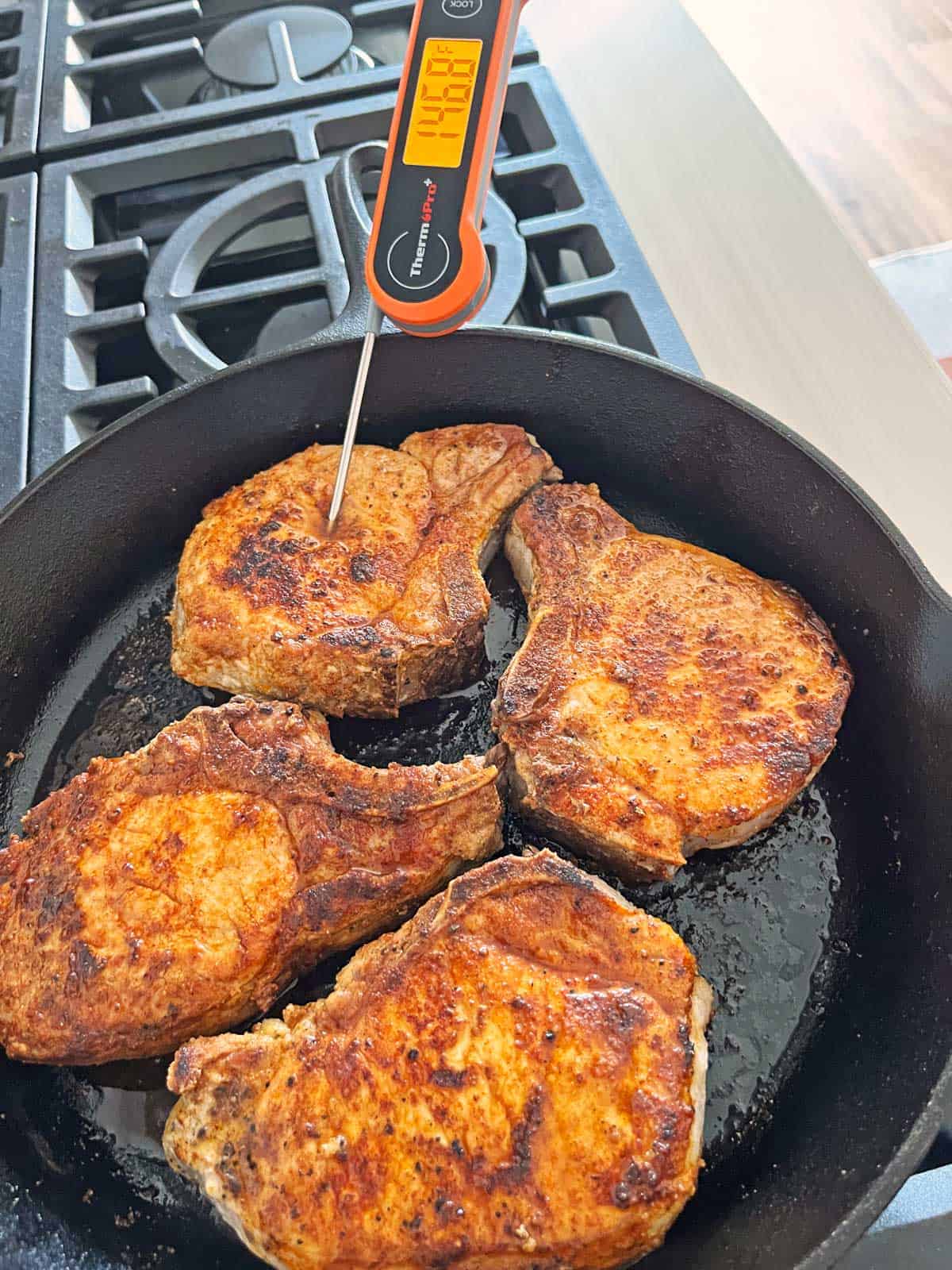 An instant-read thermometer shows that the pork chops have reached a temperature of 146.8°F.