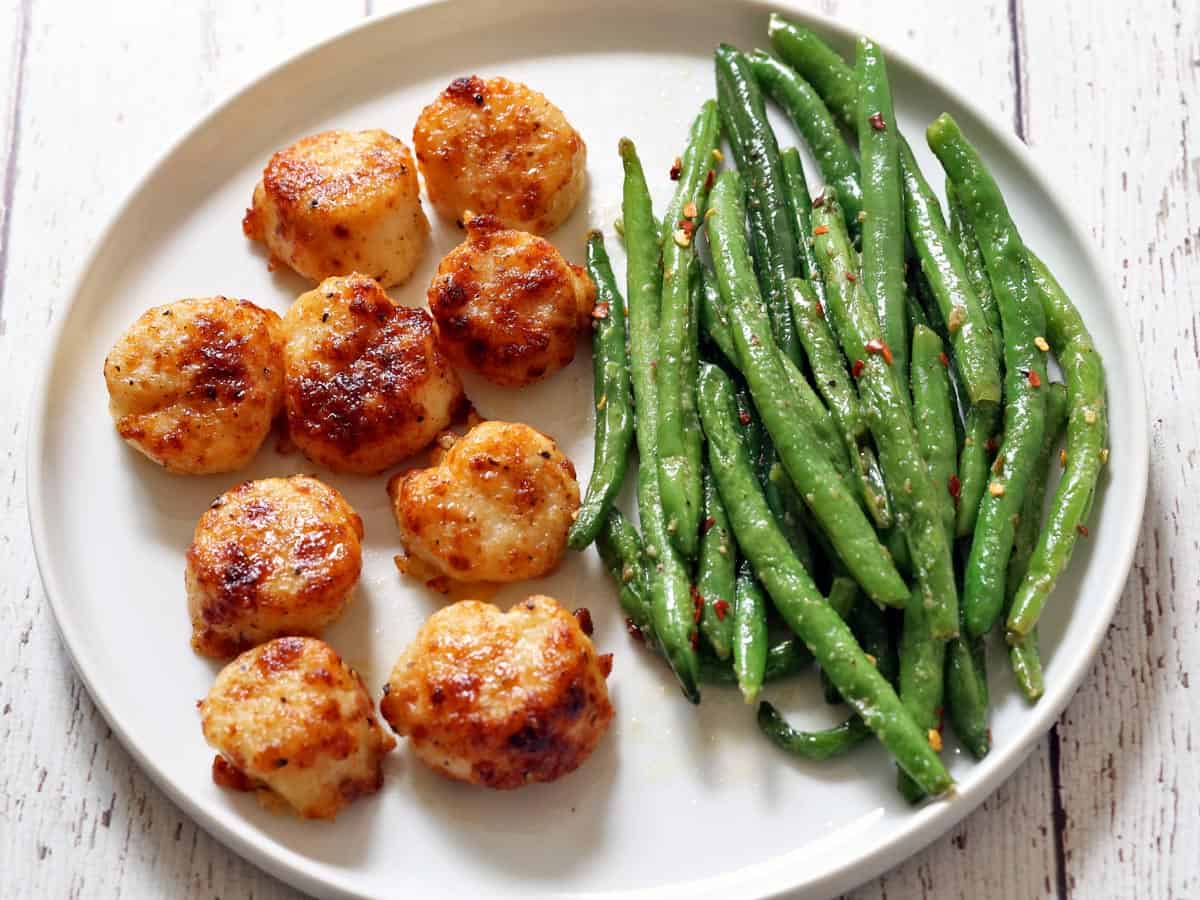 Broiled scallops are served with green beans.