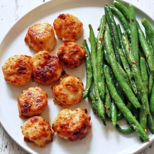 Broiled scallops are served on a white plate with green beans.