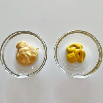 A small bowl with Dijon mustard and another with yellow mustard.