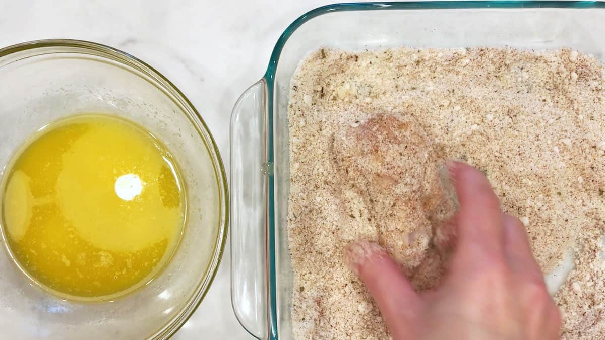 Dredging a chicken wing in grated parmesan.