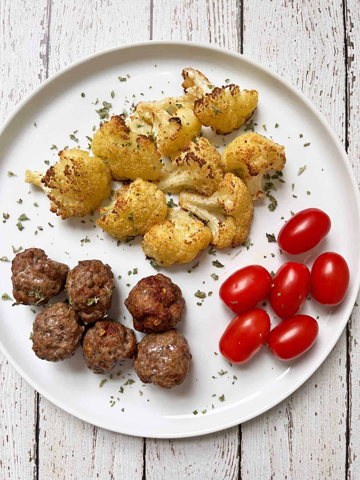 Keto meatballs are served with roasted cauliflower and tomatoes.
