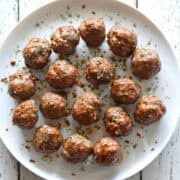 Keto meatballs are served on a white plate, garnished with red pepper flakes and dried parsley.