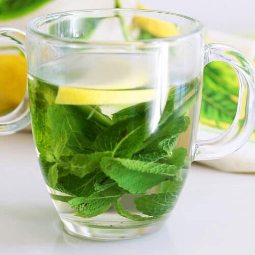 Mint tea is served in a glass mug, garnished with a slice of lemon.