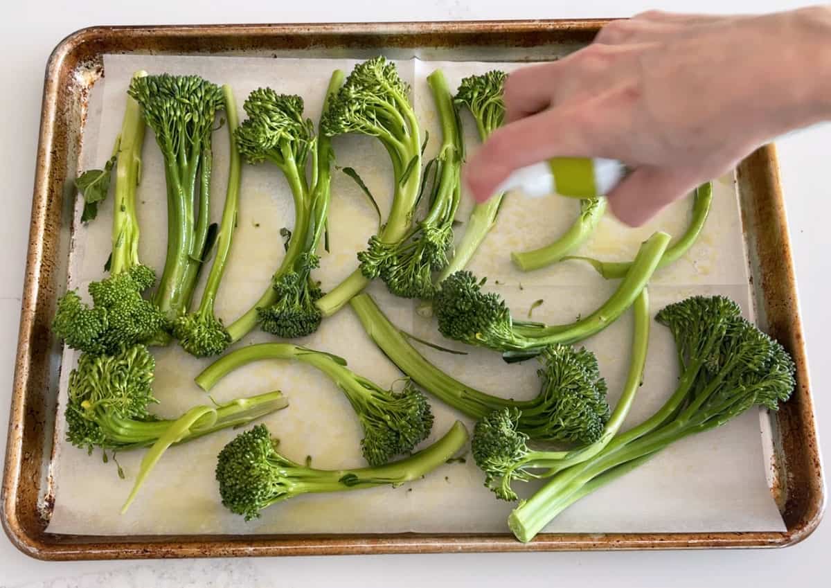 Spraying broccolini with olive oil.