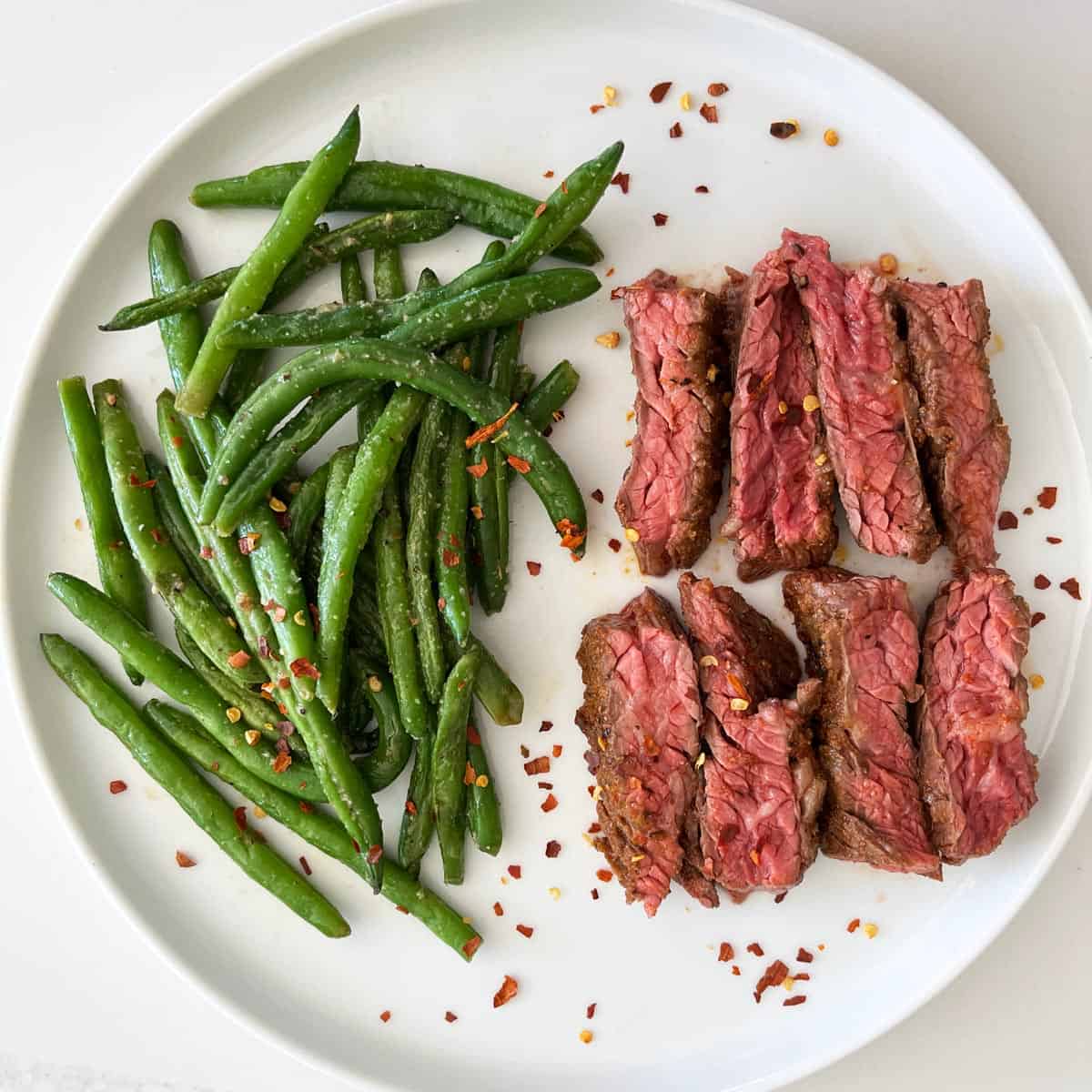 Skirt steak is served with a side of green beans.