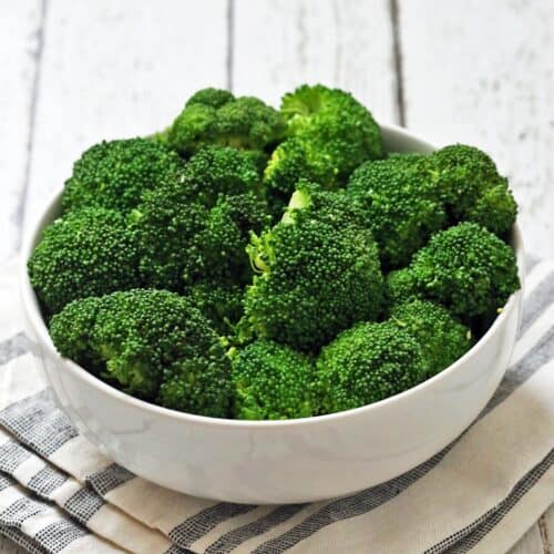 Steamed broccoli is served in a white bowl with a napkin.