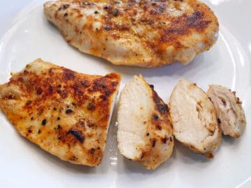 Sliced broiled chicken on a plate, showing how juicy it is.