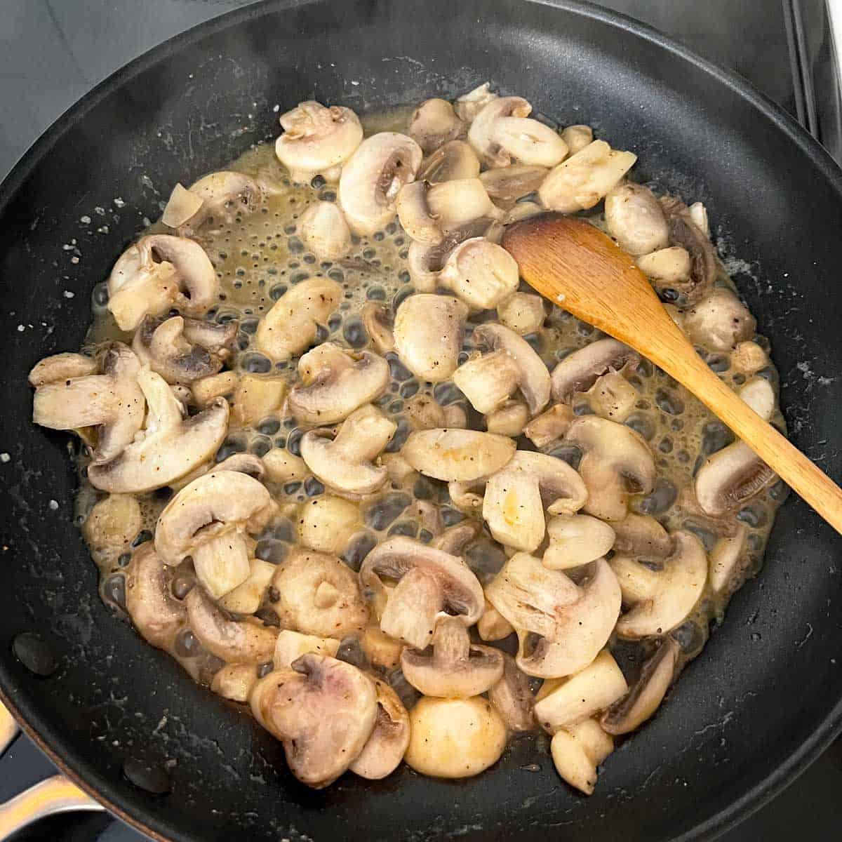 The mushrooms release liquid into the skillet.