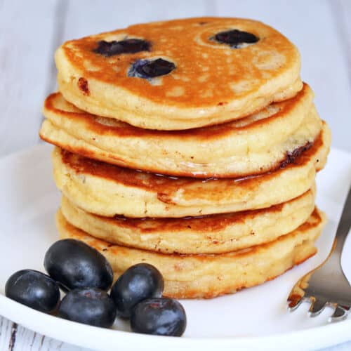 Almond flour pancakes are served on a white plate with blueberries.