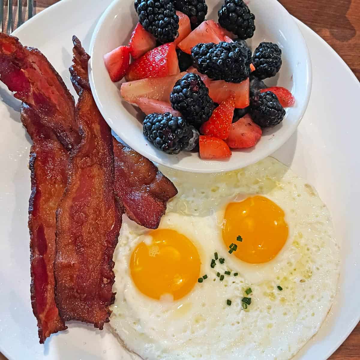 Bacon is served with fried eggs and berries.