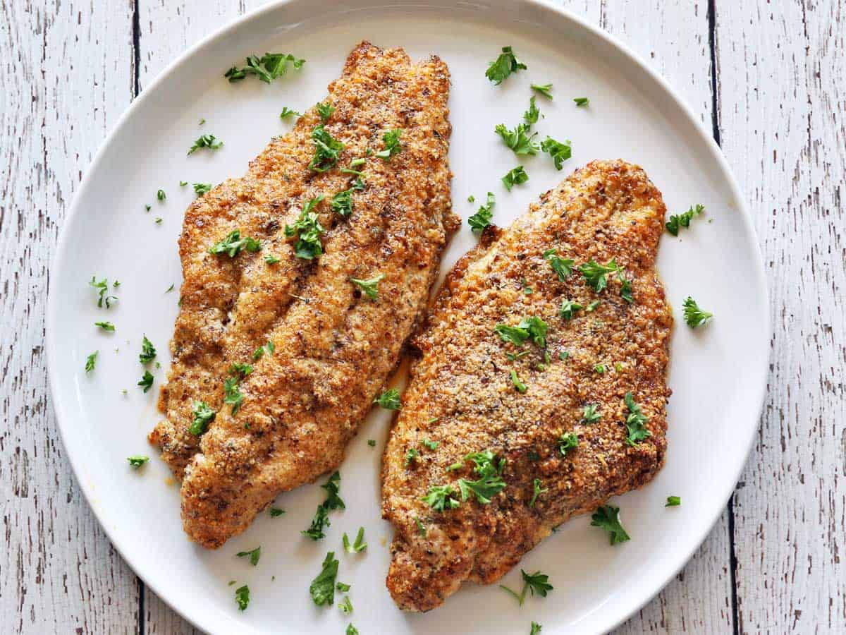 Two baked catfish fillets are served on a white plate.