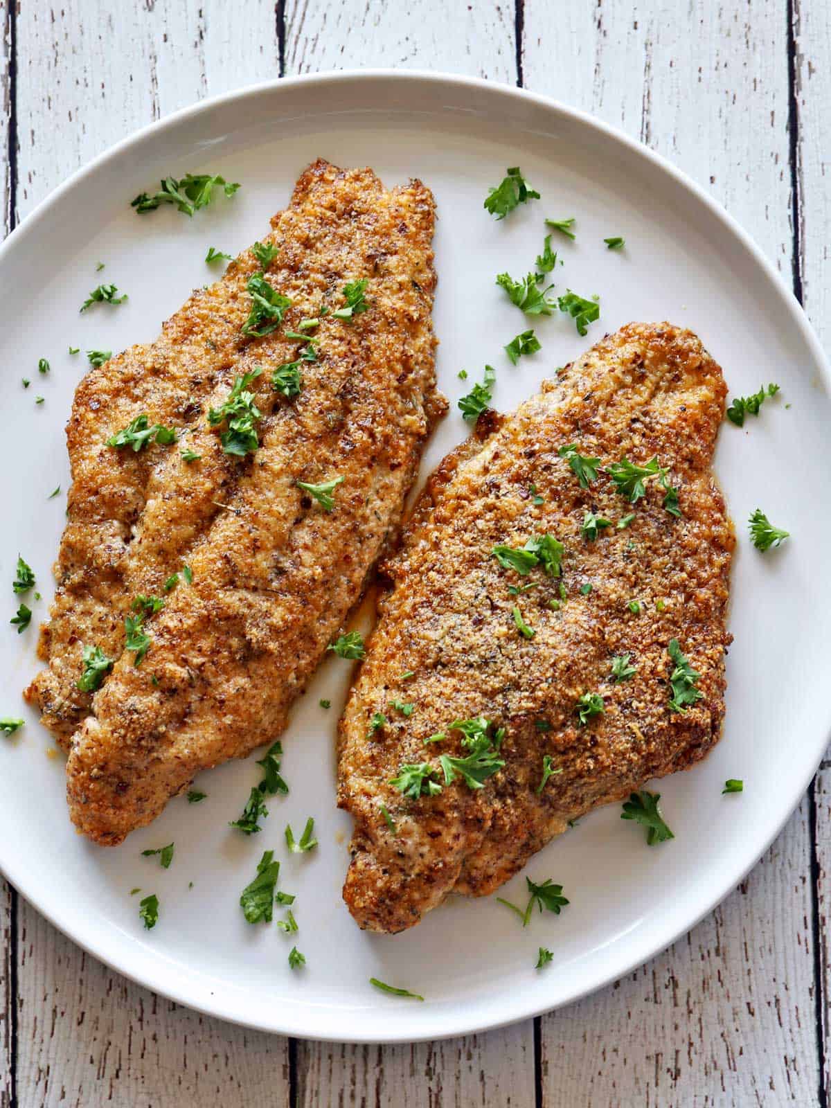 Two baked catfish fillets are served on a white plate.