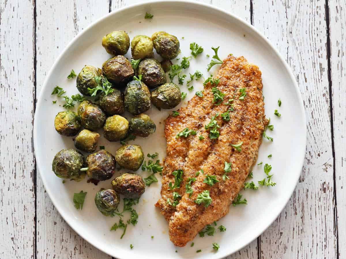 A catfish fillets is served with a side of Brussels sprouts.