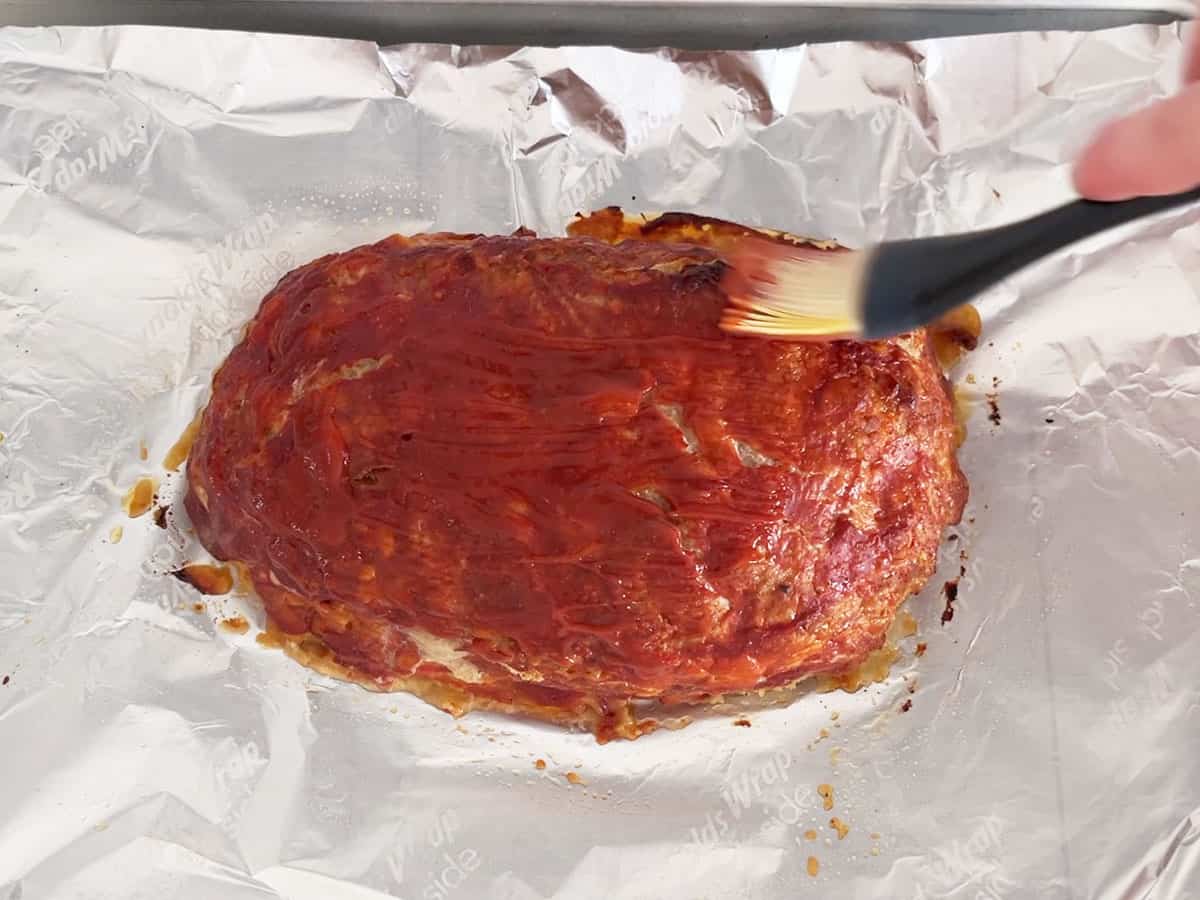 Brushing the cooked meatloaf with more ketchup.