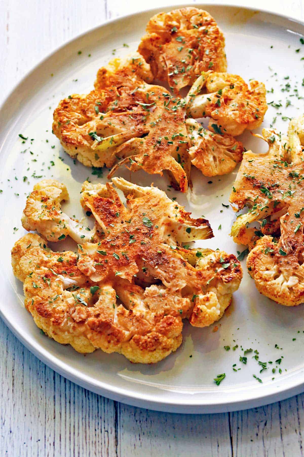 Cauliflower steaks are served on a white plate.