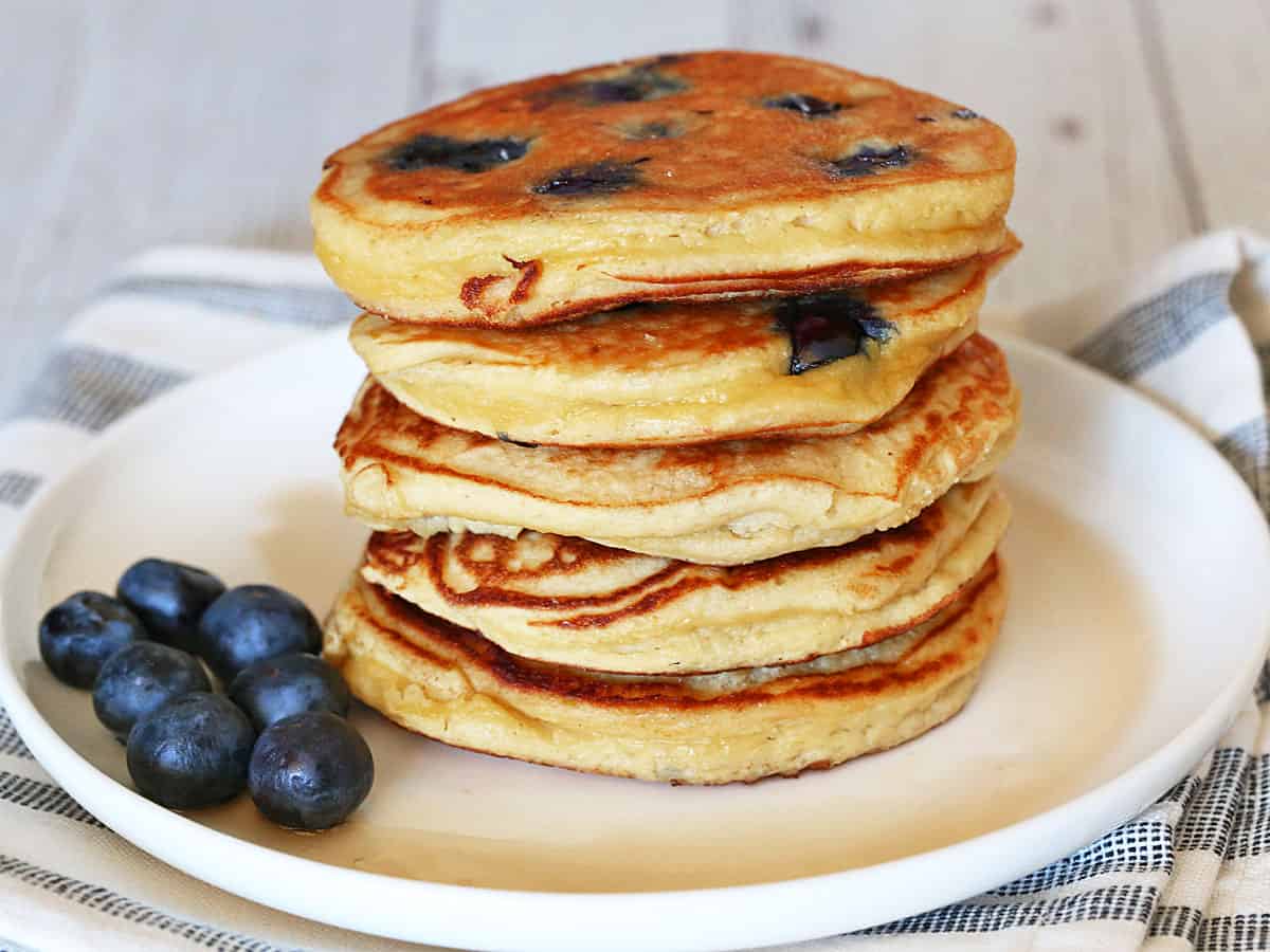 Coconut flour pancakes are stacked on a white plate.