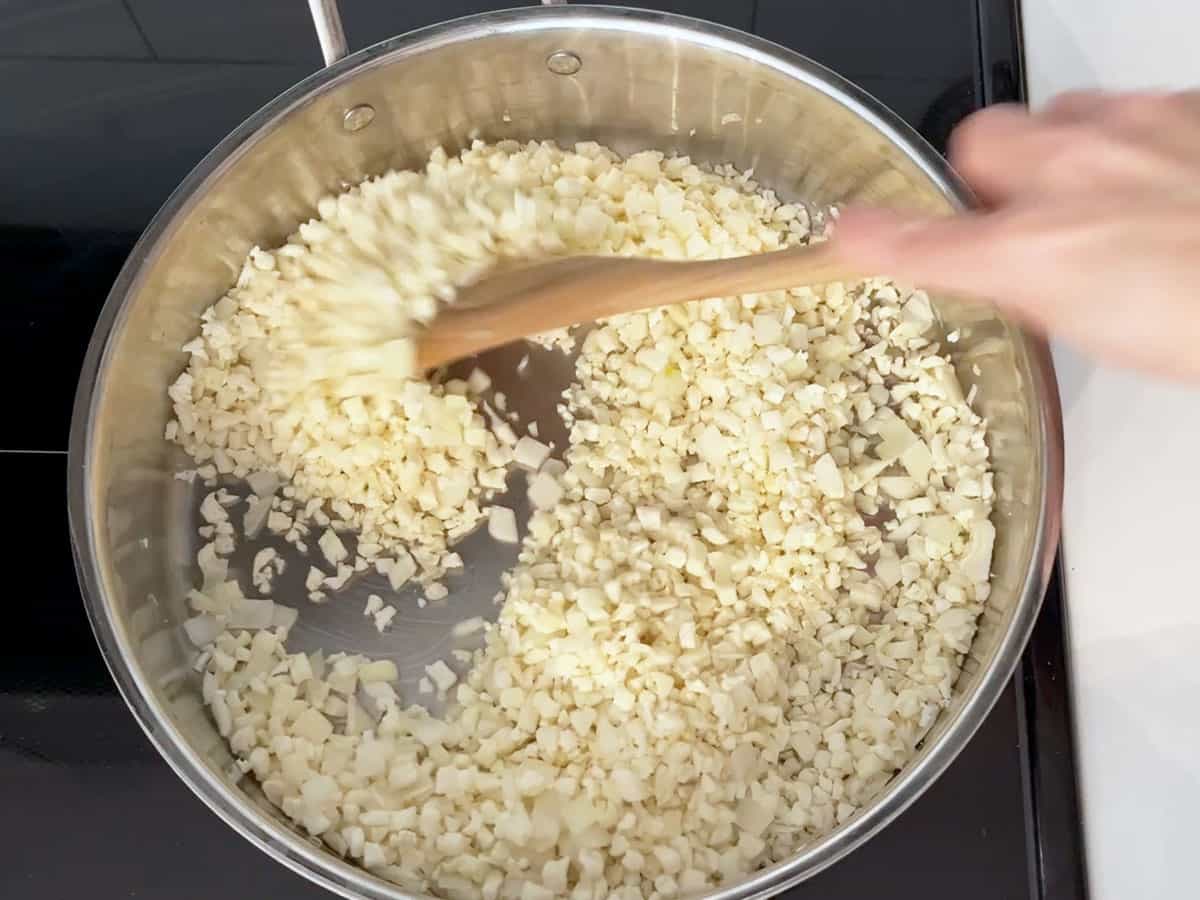 Cooking riced cauliflower and onions in a skillet.