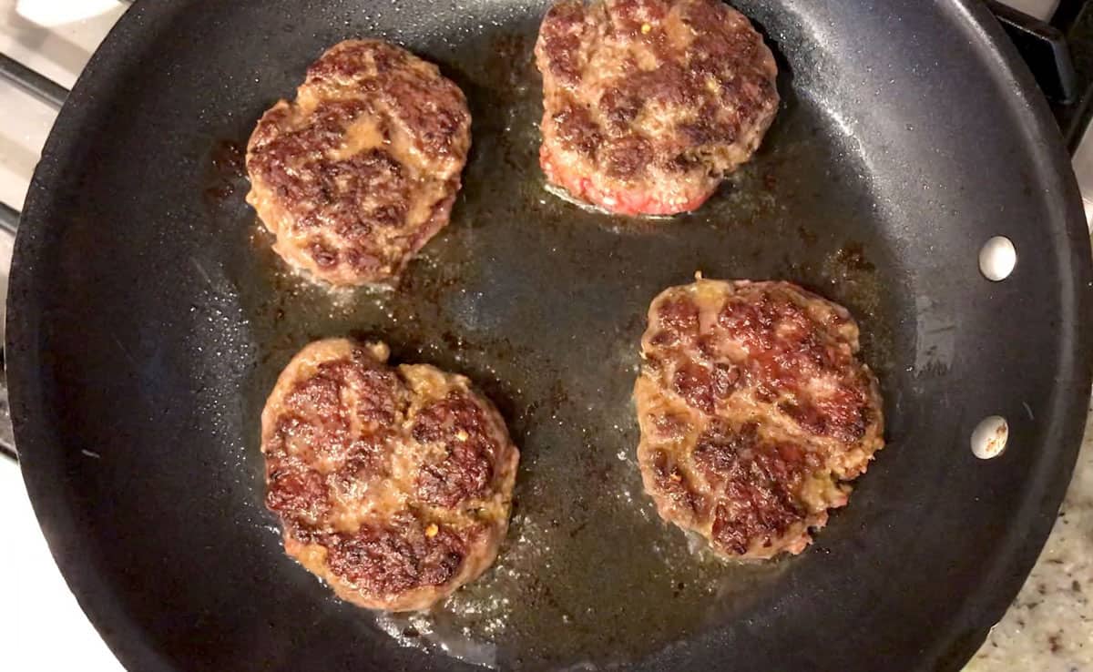 Cooking four beef sausages in a skillet.