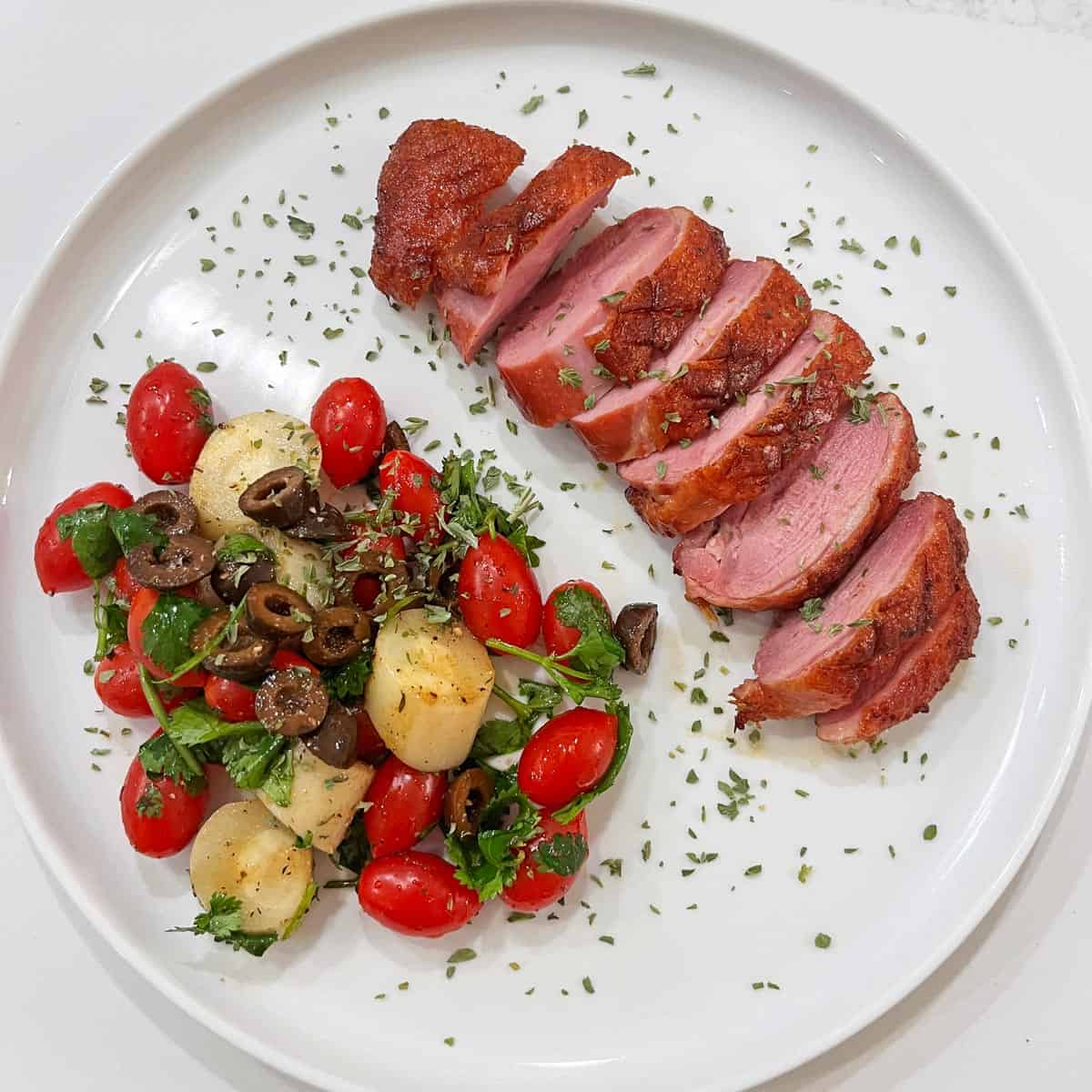 A sliced duck breast is served with a salad on a white plate.