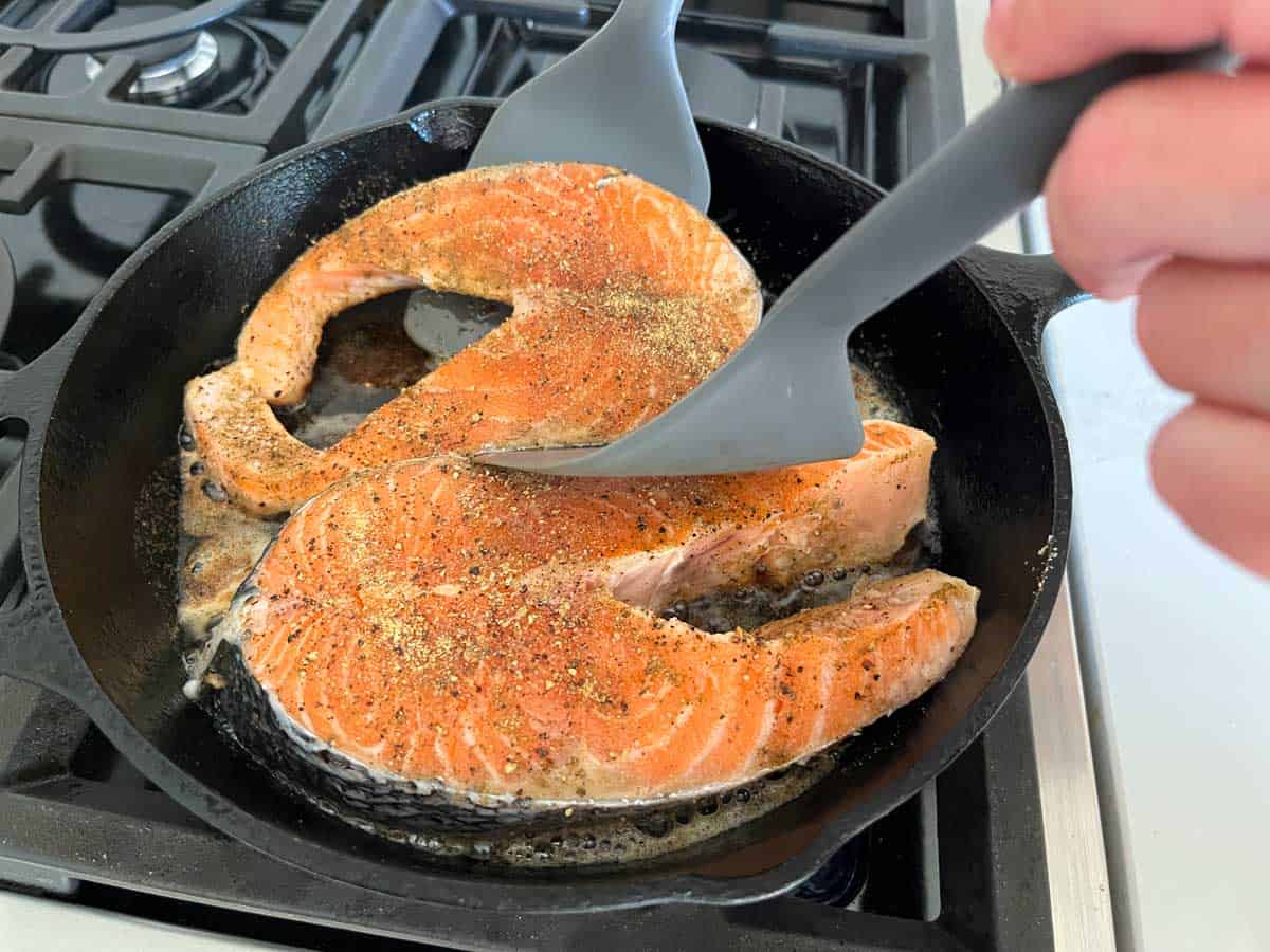 Flipping a salmon steak with two wide spatulas.