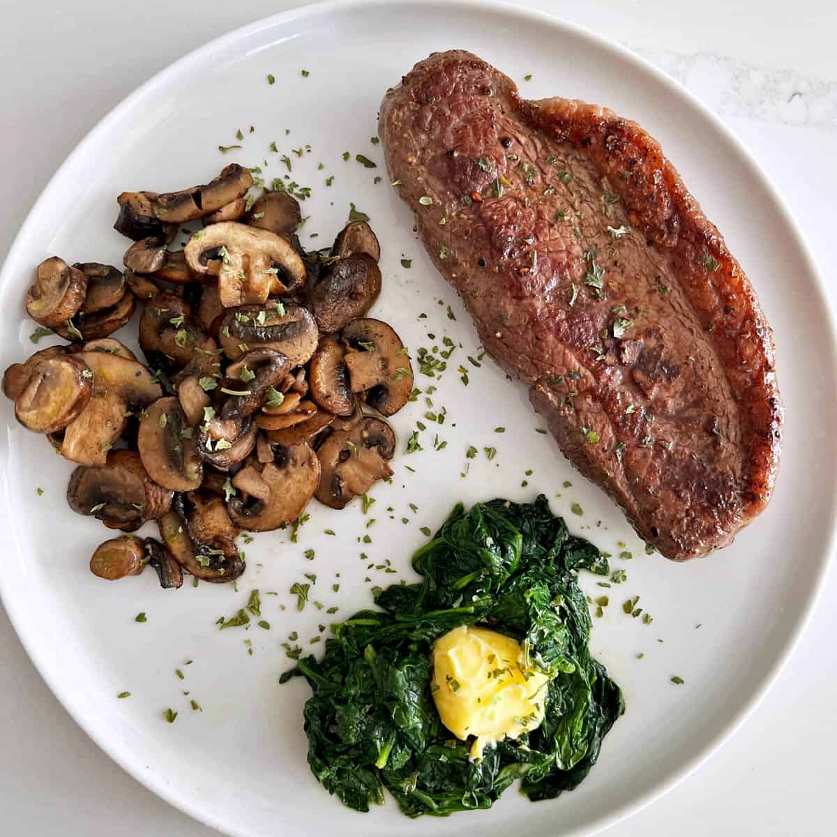 Picanha steak is served with sauteed mushrooms and sauteed spinach.