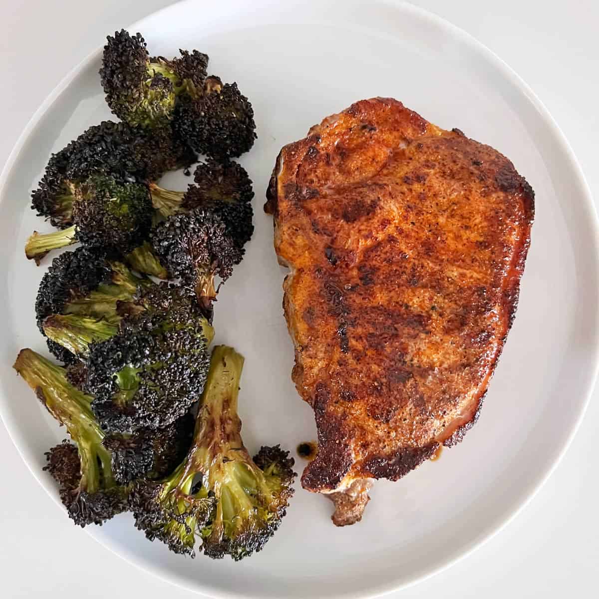 A pork chop is served with roasted broccoli.