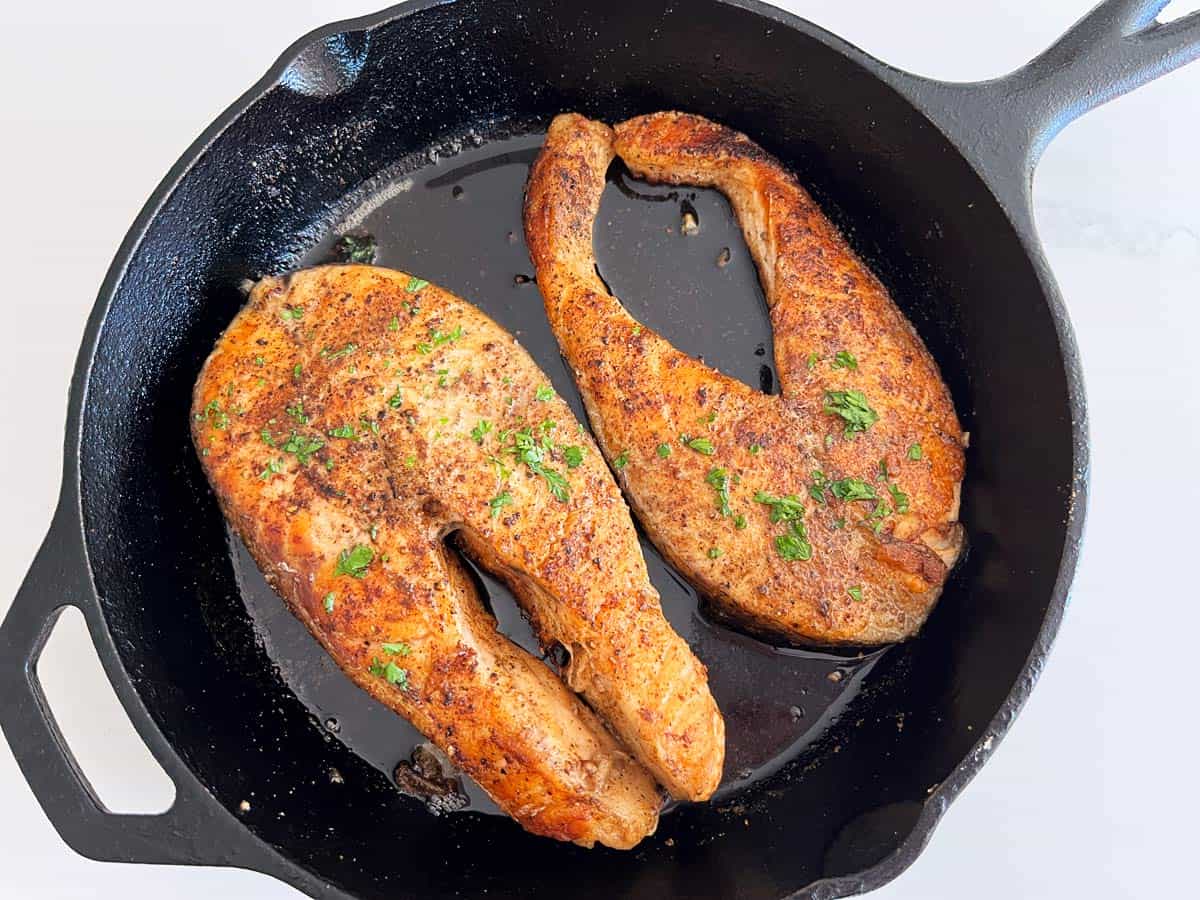 Two salmon steaks in a cast-iron skillet.
