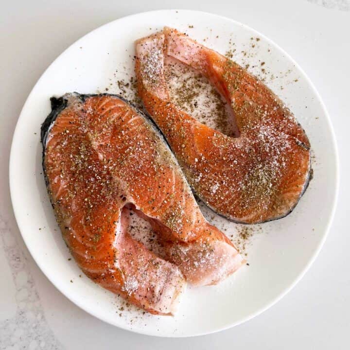 Two seasoned salmon steaks on a white plate.