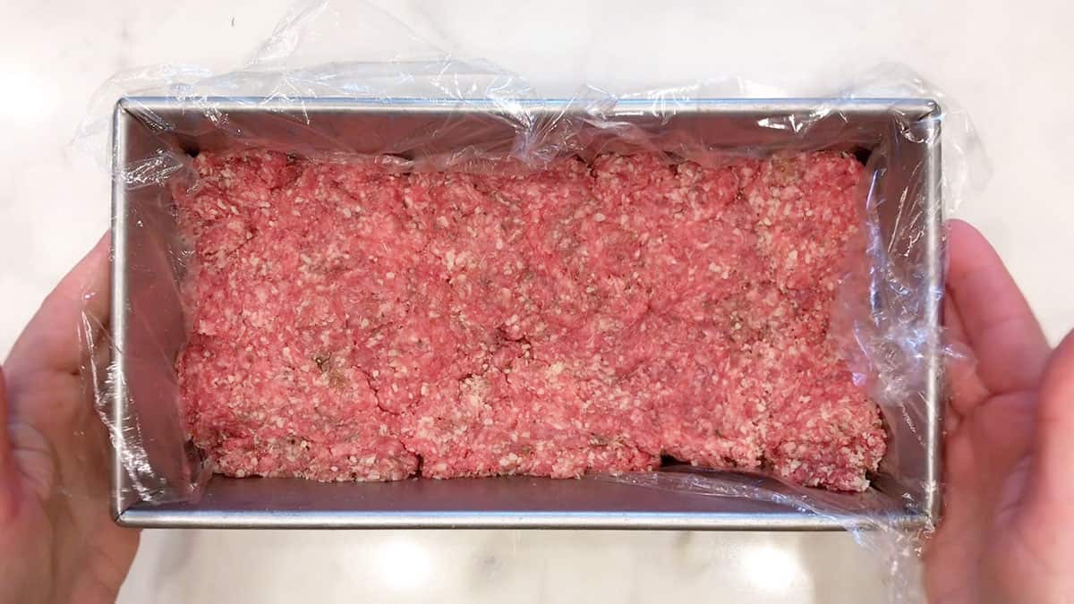 Shaping the meatloaf in a loaf pan lined with cling wrap.
