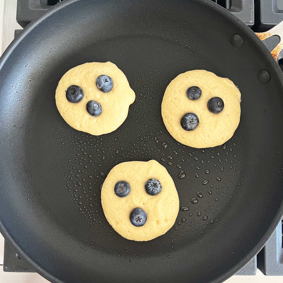 Three pancakes in a skillet, topped with blueberries.