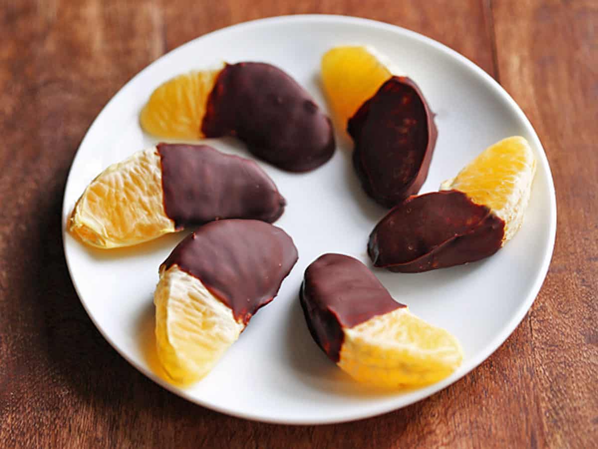 Regular orange segments are covered in chocolate and served on a white plate.