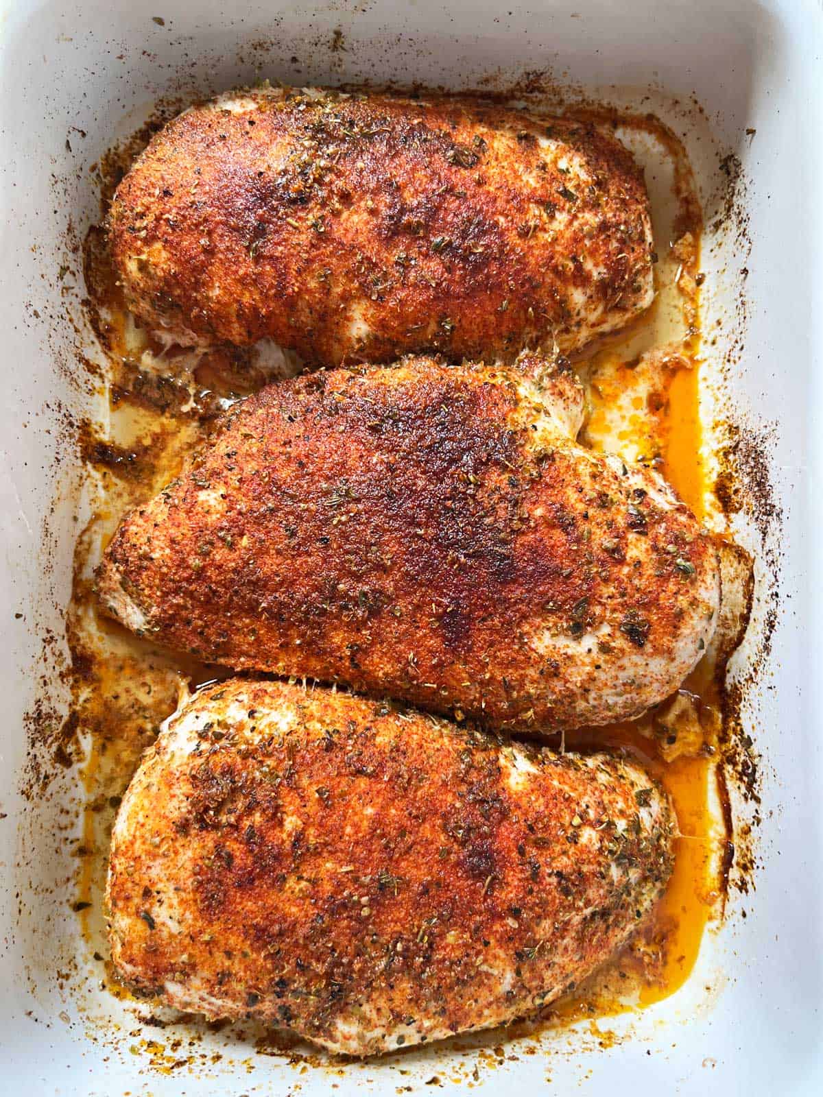 Three baked chicken breasts in a white baking dish.