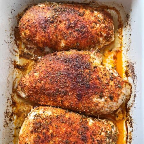 Three oven-baked chicken breasts in a white baking dish.