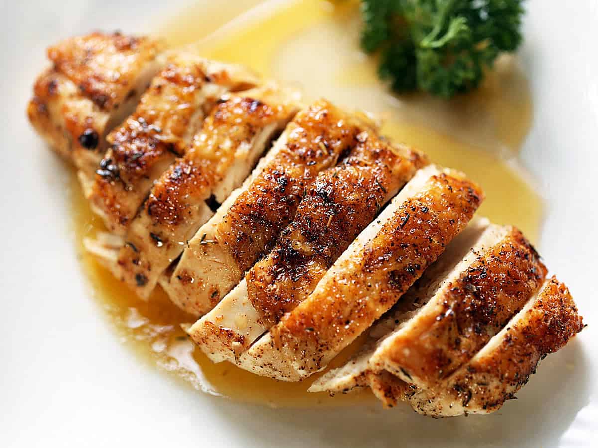 A sliced skin-on chicken breast on a white plate.