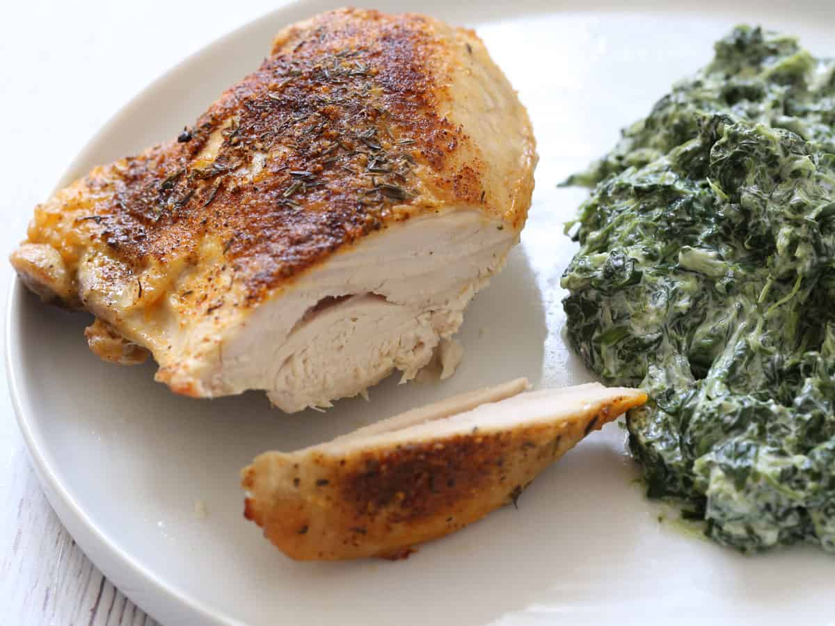 Skin-on, bone-in baked chicken breast is sliced to show it's fully cooked.