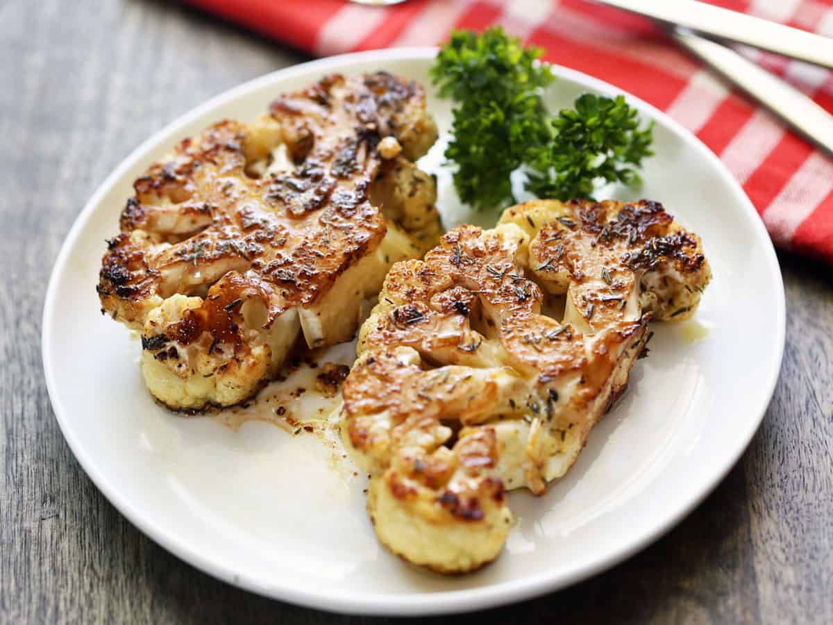 Two cauliflower steaks are coated in an olive oil and balsamic vinegar mixture.